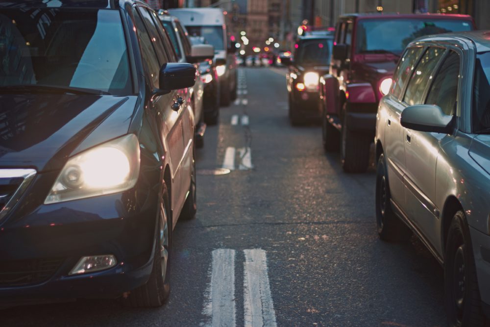 Cars are lined up in dense city traffic, packed tightly with headlights shining. Street markings guide the way as towering buildings loom in the background. In this bustling scene, it’s crucial to know professional auto accident attorneys are ready to assist when mishaps occur.