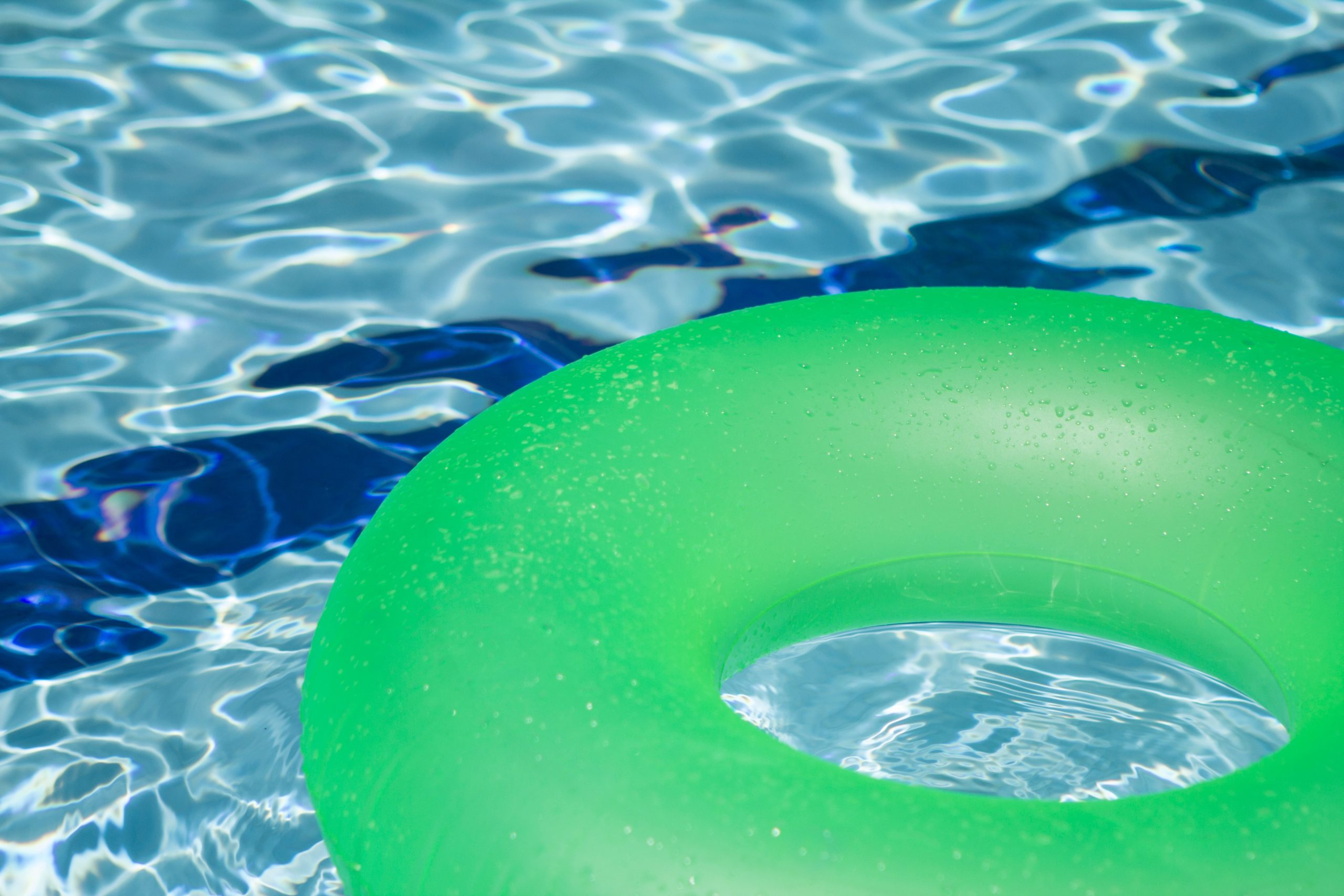 A green inflatable pool ring floats on the surface of clear blue water in a New Jersey pool, with ripples and sunlight reflections creating a serene scene.