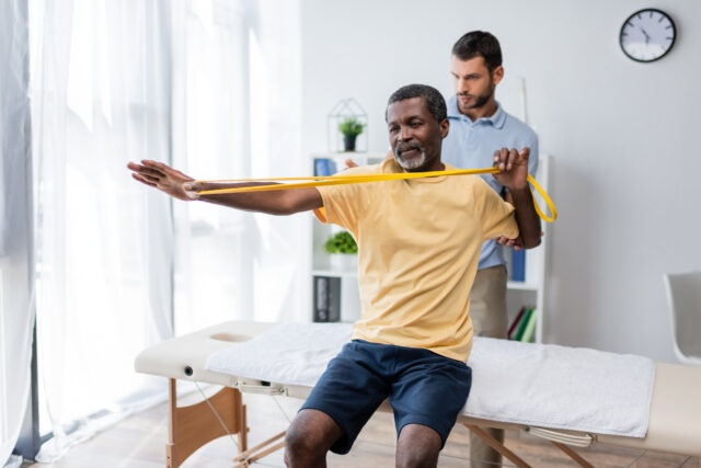 middle aged african american man sitting on massage table and physical therapy